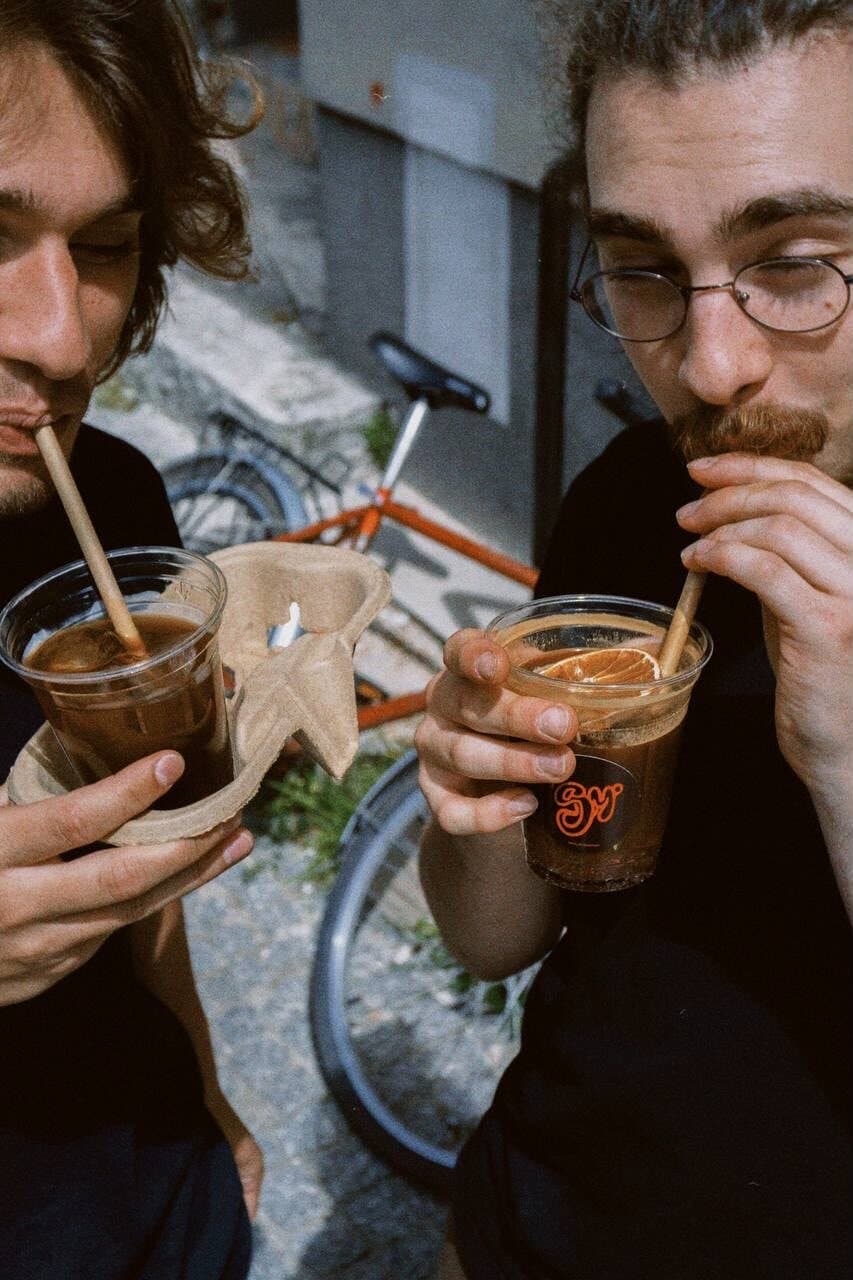 Dwie osoby piją cold brew z papierowymi słomkami przed palarnią
